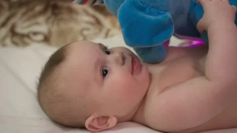 Newborn baby boy lying down, biting and playing with his toy plushy, in a cute Stock Footage 154829403