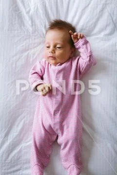 Newborn baby girl in pink striped onesie lays on duvet bed Stock Photos