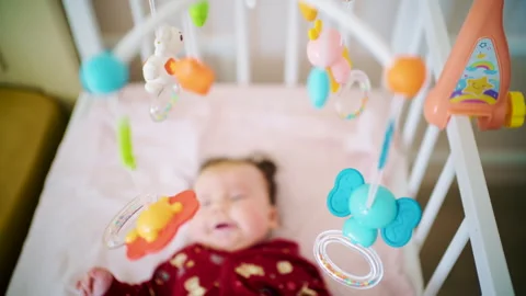 Newborn baby lying in a crib while colorful hanging toys move above Stock Footage 329387136