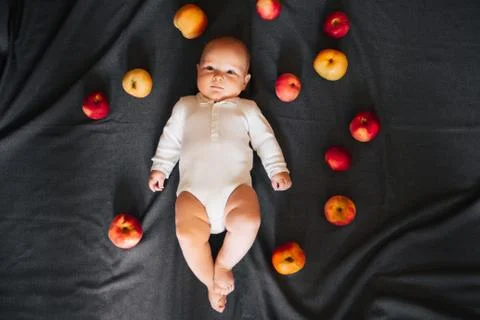 Newborn boy lying with apples. A small child in a white bodysuit Stock Photos