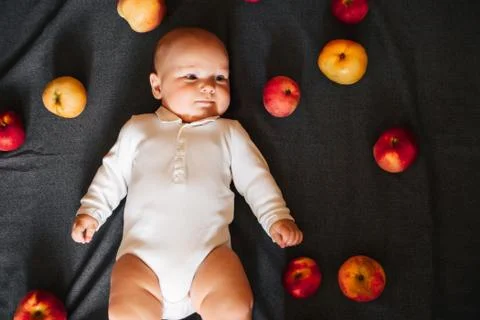 Newborn boy lying with apples. A small child in a white bodysuit Stock Photos