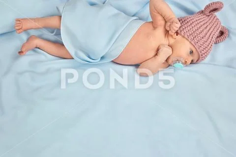 Newborn child in bed with pacifier and wool hat. Stock Photos