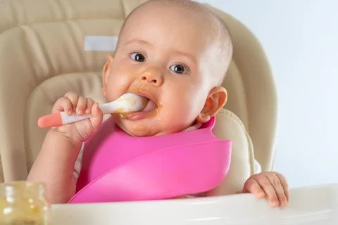 A newborn child with a spoon eats vegetable puree on his own. Stock Photos
