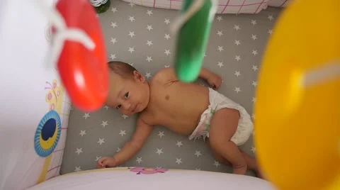 Newborn in a diaper. Top view through a colorful mobile toy elements Видео 68175589