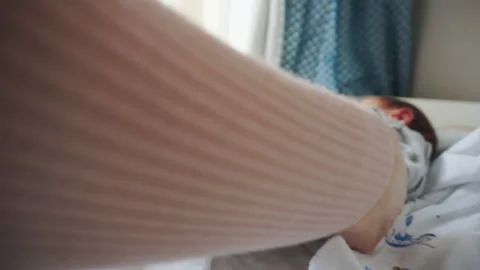 A newborn lies on a changing table by the window. Mom puts baby pants on. Caring Stock Footage 132652469