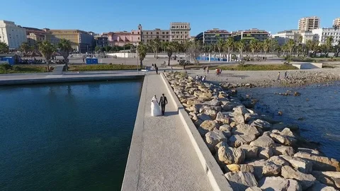 Newleywed couple walking on seafront while photo shooting Stock Footage 89780896
