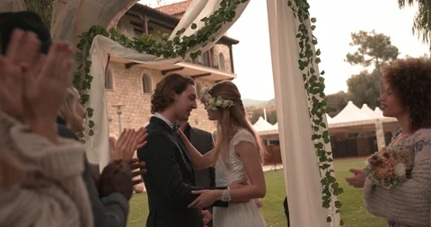 Newlywed couple kissing at rustic cottage wedding ceremony with guests Stock Footage