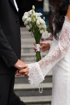 The newlyweds hold hands while the bride carries a white bouquet during a wed Stock Photos