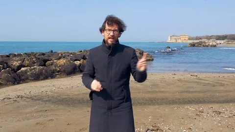 News man talking to camera in front of ocean wide shot Stock Footage 101542926