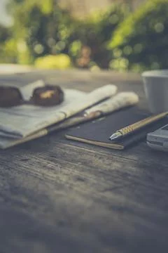Newspaper, a notebook and cup of coffee on a wooden table outside Stock Photos
