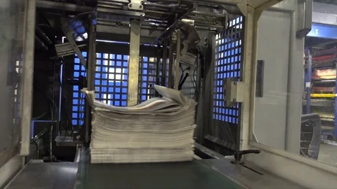 Newspaper stack lowers to printing press conveyor belt then toward Stock Footage 128862367