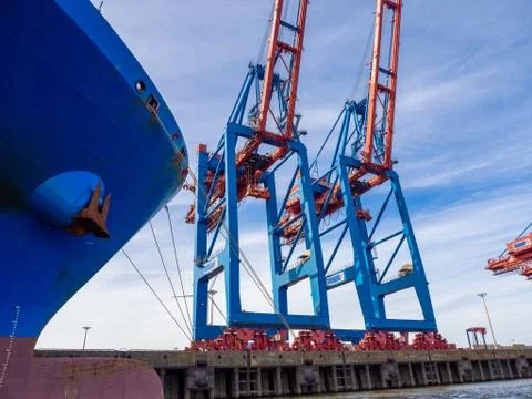 Next to a container ship there are large container cranes for loading and unl Stock Photos