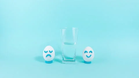 Next to half-filled glass, two eggs appear with cheerful and sad expression. Stock Footage 220230430