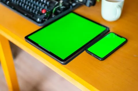 Next to an old typewriter lies a tablet  with a green screen on the table, a  Stock Photos