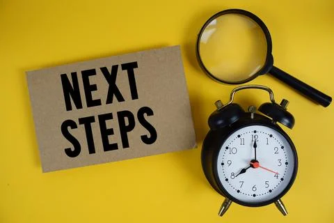 Next Steps text written on paper with magnifying glass and alarm clock on y.. Stock Photos