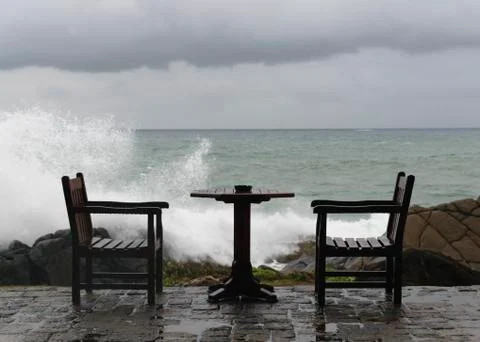 Ngry waves crash over rocks on the coast near abandoned tables Stock Photos