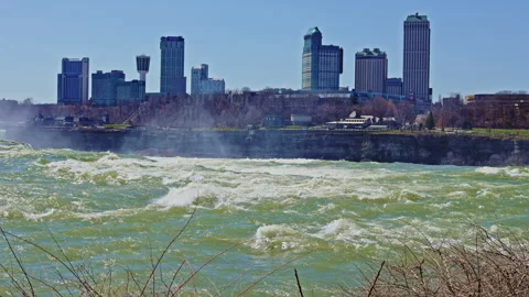 Niagara Falls with city skyline in the background on a sunny day showing fast Stock Footage 334158467