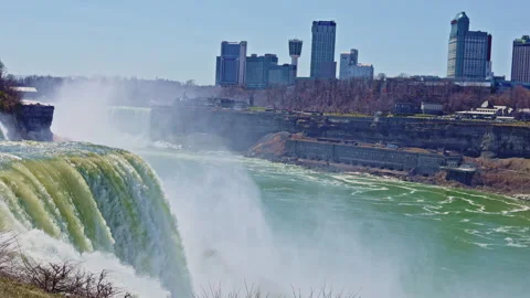 Niagara Falls flows into the river while buildings and city skyline are visible Stock Footage 334158463