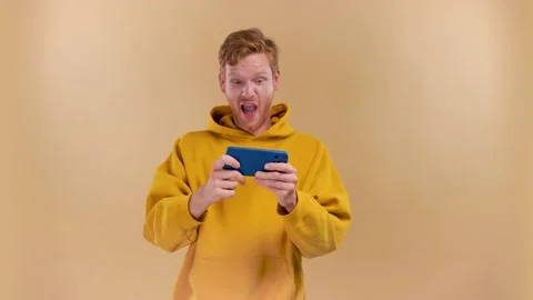 Nice addicted cheerful guy using gadget playing network game on a beige Stock Footage 198325360