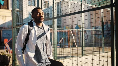 Nice African guy in modern clothes walking near sports ground with beautiful Stock Footage 92054190