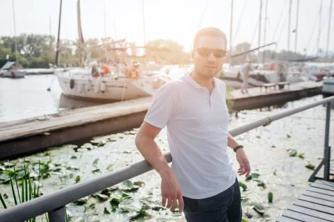 Nice and handsome guy stand on pier and lean to railing. He looks on camera. Guy Stock-Fotos