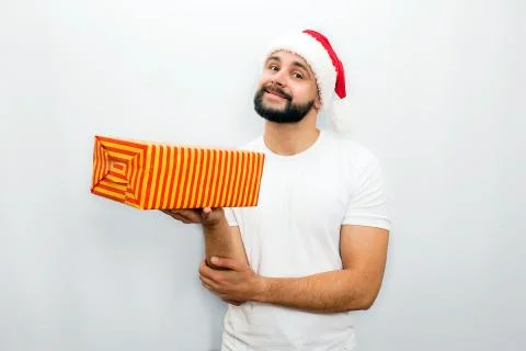 Nice bearded man in red hat stands and holds orange box with present in one hand 写真素材