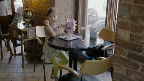 Nice blonde girl looking at icecream, eating and showing it in a café in slo-mo Stock Footage 105150341