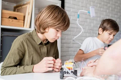 Nice boy in green shirt constructing a robot car at workshop Stock Photos