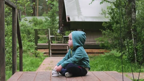 Nice boy of two years in a blue waistcoat and cap sits in a park on a bench and Stock-Footage 133328307