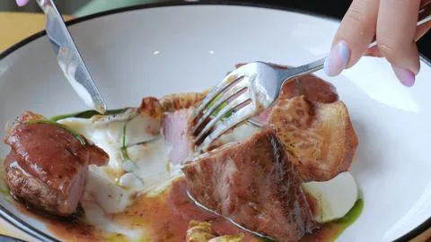 A nice brunette in a restaurant eats a dish of meat and chips with pleasure Stock Photos