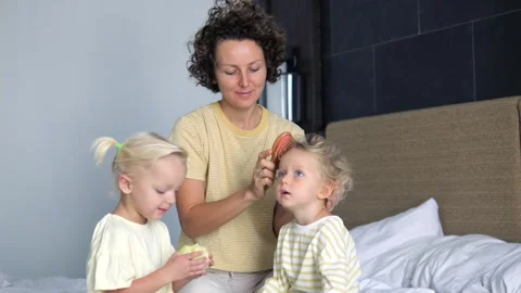 NIce caring caucasian mother combs her daughters' hair while sitting on bed. Mom Stock Footage 240111978