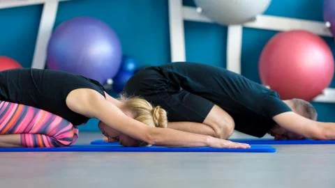 Nice couple doing yoga in a studio. Young people in yoga class in Hare pose.  Stock Photos