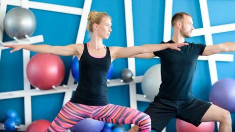 Nice couple doing yoga in a studio. Young people in yoga class in Warrior pos Stock Photos