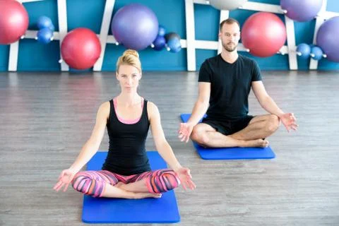 Nice couple doing yoga in a studio. Young people in yoga class in lotus posit Stock Photos