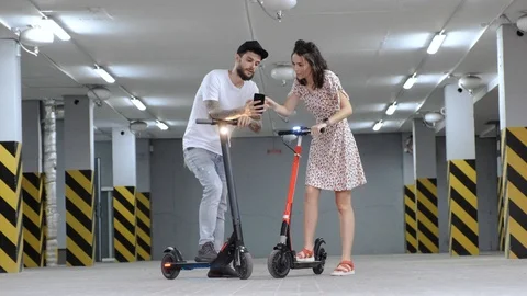 Nice couple rides forward electric scooters in parking lot Stock Footage