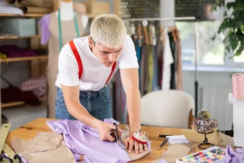 Nice creative young guy designer cutting material or textiles at sewing atelier Stock Photos