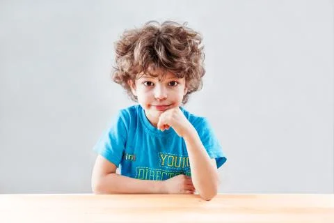 The nice curly-headed kid having propped up the head with a smile looks in th Stock Photos
