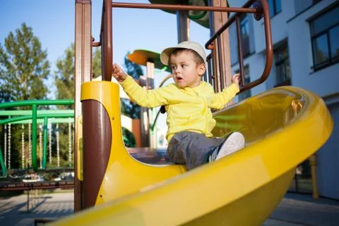 Nice cute boy of three years in a yellow jacket is playing on a bright playgr Stock Photos
