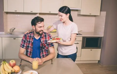 Nice giel stands besides guy and give him plate with omlet and cherry tomatoes Stock Photos