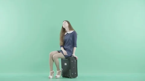 A nice girl in dress sits on the suitcase Stock Footage