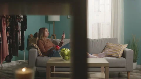 Nice girl eats a red apple, lying on sofa and and speaks via video link Stock Footage 151977446