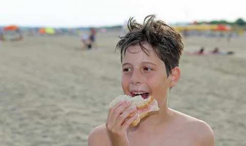 Nice guy while eating a big sandwich on the beach in summer Фото