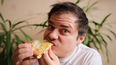Nice guy in a white T-shirt eats delicious cheese pizza with great pleasure Stock-Footage 149314316