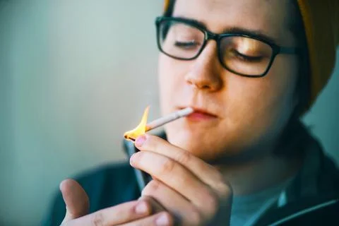 A nice guy in a yellow cap and black-rimmed glasses lights a cigarette with a Stock Photos