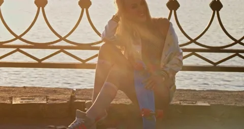 Nice lady is posing sitting on waterfront parapet with skateboard 스톡 동영상 145527165