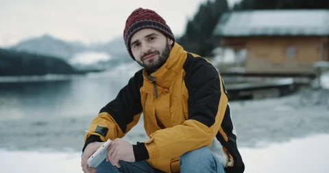Nice looking man in a orange jacket sitting on a blue boat beside of a shore Stock Footage 101293828
