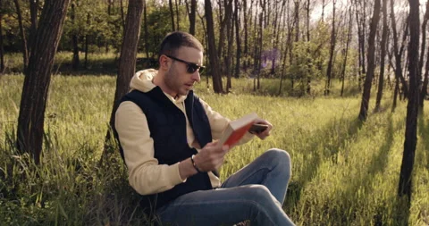 A nice man reads a book sitting on the grass in the park Stock Footage 131179452