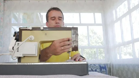 A nice man is sitting at the electric sewing machine at home. He sews several Stock Footage 78621613