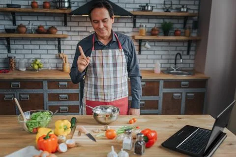 Nice man stand at table in kitchen. He look at colorful vegetables and smile Фото