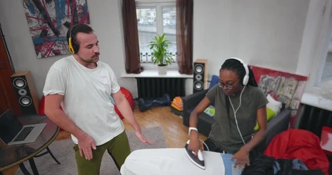 Nice smiling couple dancing together and irons clothes Stock Footage 99322597